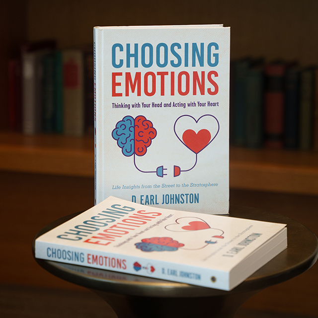 Book cover 'Choosing Emotions' with a brain–heart illustration and the tagline 'Thinking with Your Head and Acting with Your Heart' on display in a library setting.